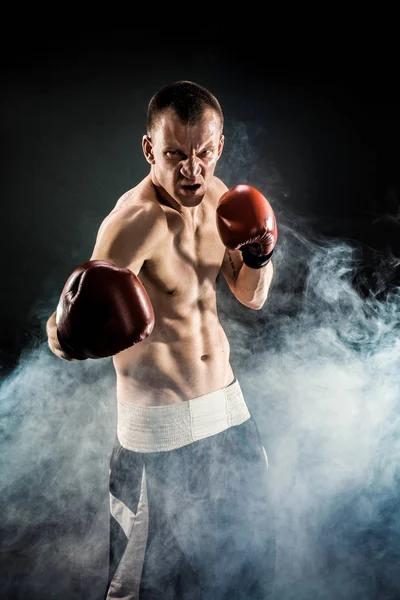 Muscular kickbox o muay thai luchador puñetazos en el humo . — Foto de Stock