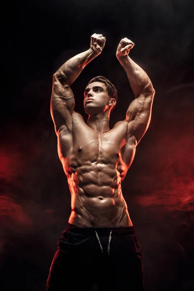 Sterke bodybuilder man met perfecte abs, schouders, biceps, triceps, borst poseren in rook handen omhoog. — Stockfoto