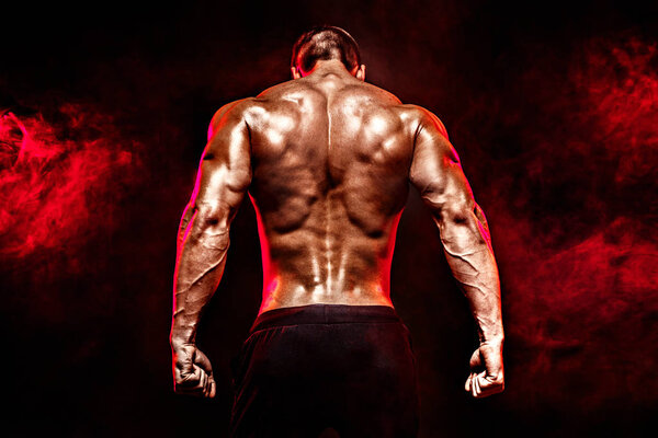 Back view of Unrecognizable man, strong muscles posing with arms down in smoke.