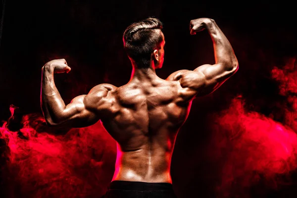 Vista posterior del hombre irreconocible, músculos fuertes posando con los brazos levantados en humo . — Foto de Stock