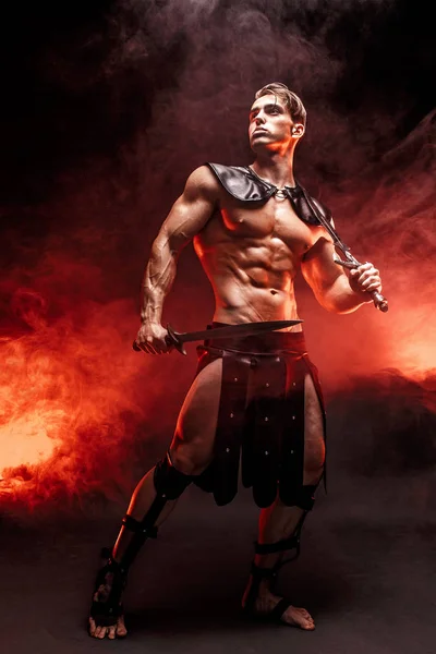 Полнометражный портрет сексуального молодого воина, держащего меч и отводящего взгляд, позируя против огня. Copyspace — стоковое фото