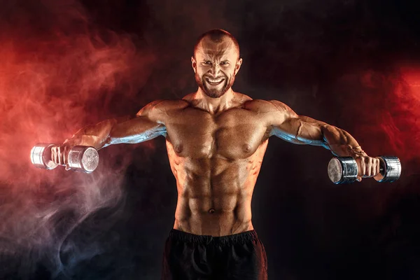 Fuerte deportista levantando pesada mancuerna en el humo — Foto de Stock