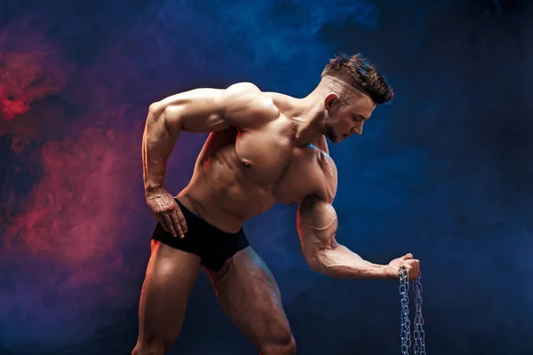 Stilig power atletisk man kroppsbyggare gör övningar med kedja. Konditionen muskulös kropp på mörka rökiga bakgrund. Perfekta hane. Awesome bodybuilder, poserar. — Stockfoto