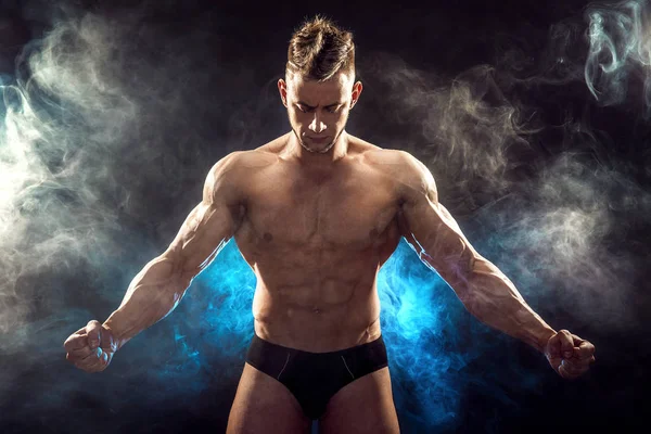 Knappe macht atletische man bodybuilder. Fitness gespierd lichaam op donkere rook achtergrond. Perfecte man. Awesome bodybuilder, poseren. — Stockfoto