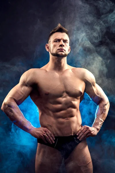 Hermoso poder atlético hombre culturista. Cuerpo muscular fitness sobre fondo de humo oscuro. Hombre perfecto. Impresionante culturista, posando . — Foto de Stock