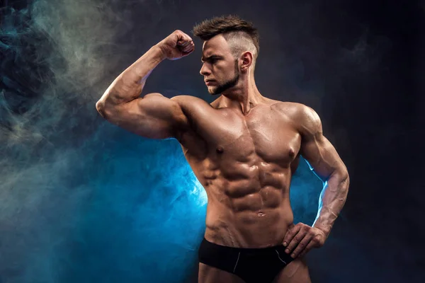 Όμορφος δύναμη αθλητική άντρας bodybuilder. Υγρή Fitness μυώδες σώμα σε σκούρο φόντο καπνού. Τέλειο αρσενικό. Φοβερό bodybuilder, θέτοντας. — Φωτογραφία Αρχείου