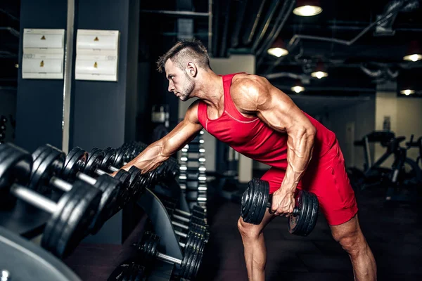 Culturista determinado levantando pesadas mancuernas negras en el gimnasio . — Foto de Stock