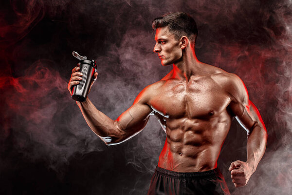 Muscular man with protein drink in shaker over dark smoke background