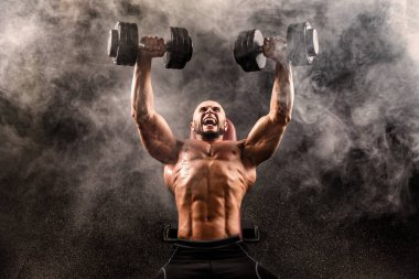 Kel üstsüz kaslı adam Bench Press duman üzerinde iki Dumbbells ile yapıyor