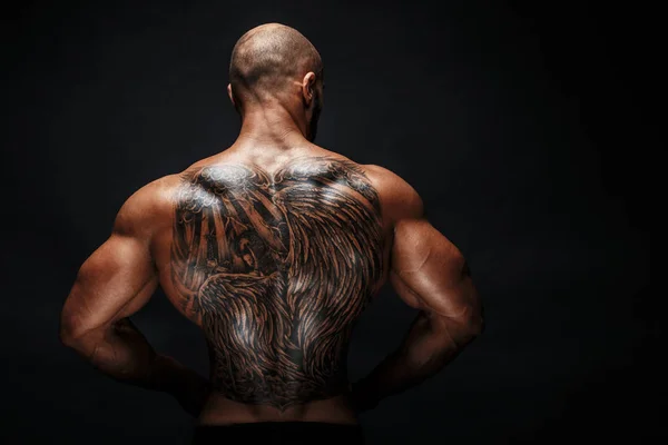 Unrecognizable muscular man with tattoo on back against of black background. Isolated. — Stock Photo, Image