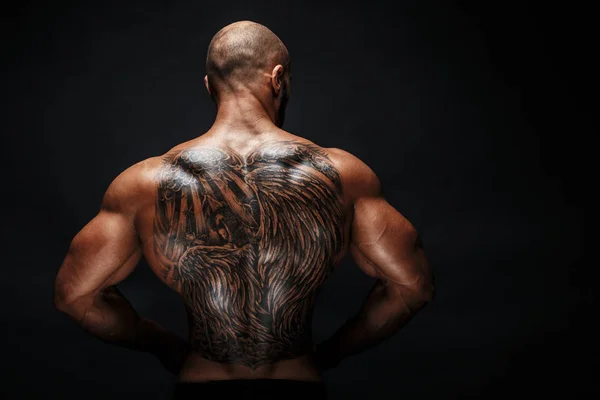 Homem musculoso irreconhecível com tatuagem nas costas contra fundo preto. Isolados . — Fotografia de Stock