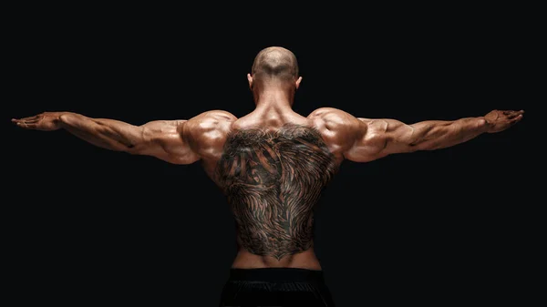 Back view of tattoed bodybuilder with outstretched arms — Stock Photo, Image