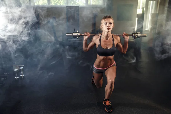 Young sexy girl in the gym doing squat on smoke background — Stock Photo, Image