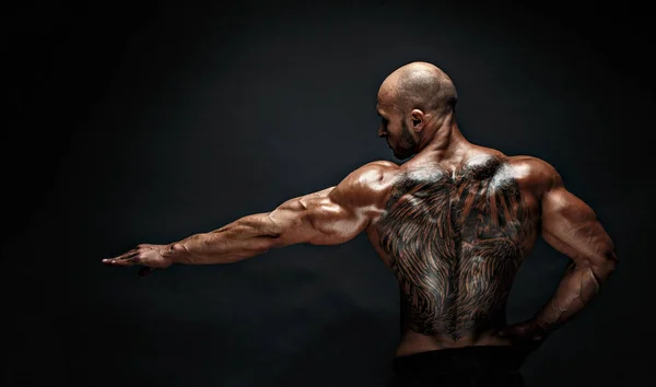 Uomo muscoloso irriconoscibile con tatuaggio sulla schiena su sfondo nero. Isolato . — Foto Stock