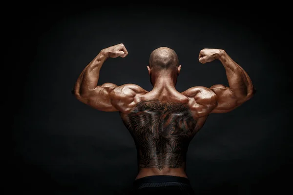 Ugjenkjennelig muskuløs mann med tatovering på ryggen mot svart bakgrunn. Isolert . – stockfoto