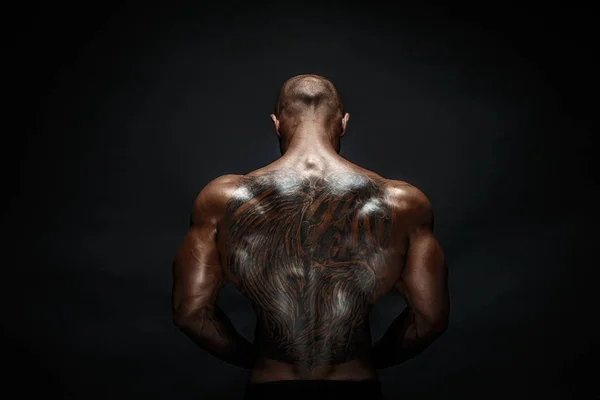 Homem musculoso irreconhecível com tatuagem nas costas contra fundo preto. Isolados . — Fotografia de Stock