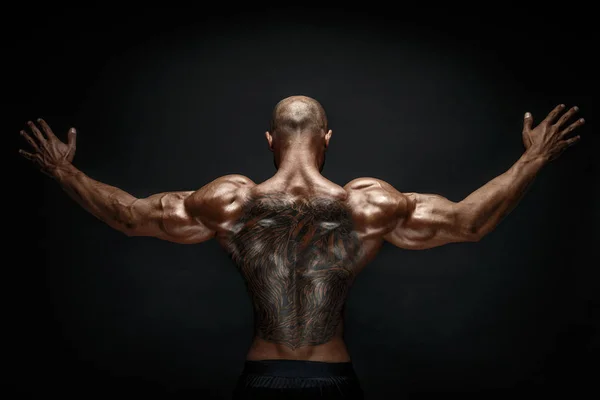 Unrecognizable muscular man with tattoo on back against of black background. Isolated. — Stock Photo, Image