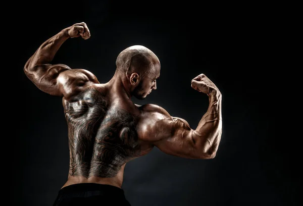Uomo muscoloso irriconoscibile con tatuaggio sulla schiena su sfondo nero. Isolato . — Foto Stock