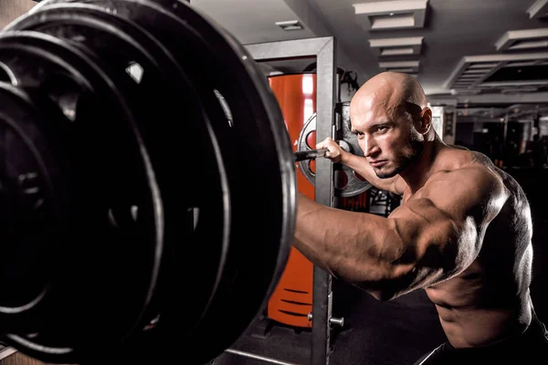 Bald Bodybuilder preparing for exercise with barbell in gym