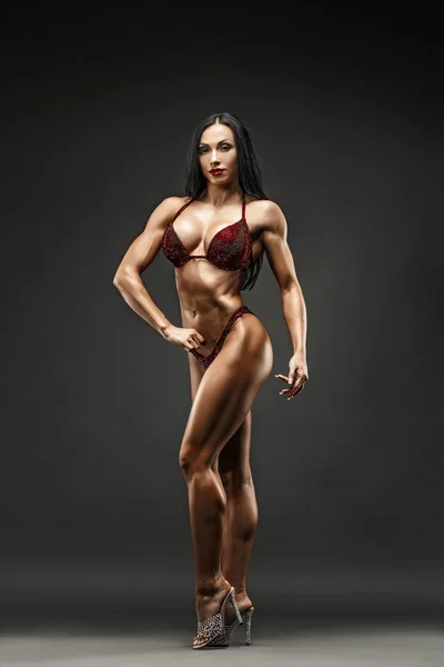 Strong and muscular sports girl in bikini posing against camera in studio