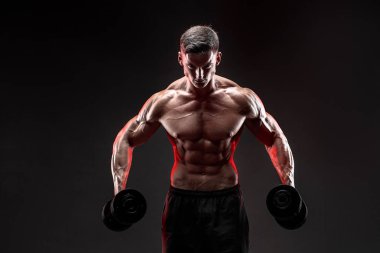 Konsantre olmuş kaslı adam dambılla egzersiz yapıyor.