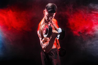 Konsantre olmuş kaslı adam dambılla egzersiz yapıyor.