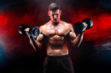 Konsantre olmuş kaslı adam dambılla egzersiz yapıyor.