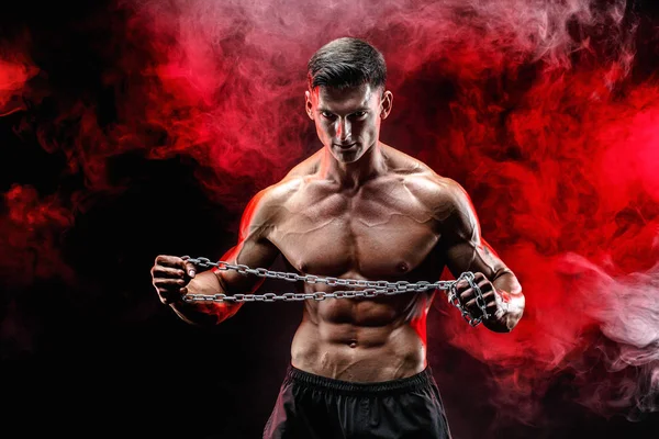 Retrato de deportista musculoso rasgando cadena de metal. Fondo negro con humo rojo — Foto de Stock