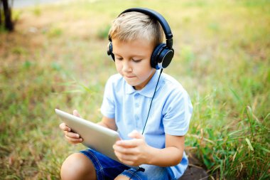 Ormandaki kulaklık giyen ve tablet PC'de oyun oturan genç çocuk.