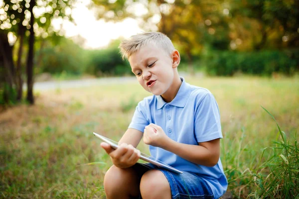 若い子供 sittingin 中庭とタブレット pc でゲームをプレイ. — ストック写真