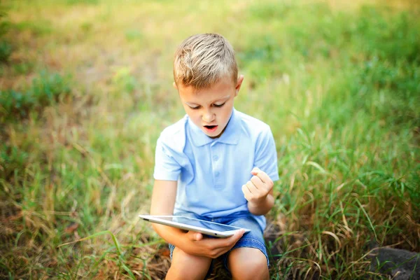 Młode dziecko sittingin dziedziniec i granie w gry na komputerze typu tablet. — Zdjęcie stockowe