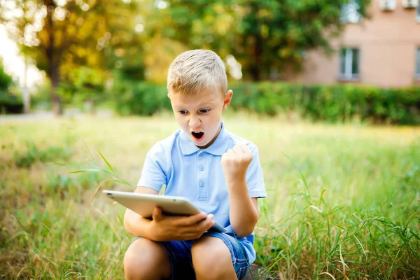 若い子供 sittingin 中庭とタブレット pc でゲームをプレイ. — ストック写真