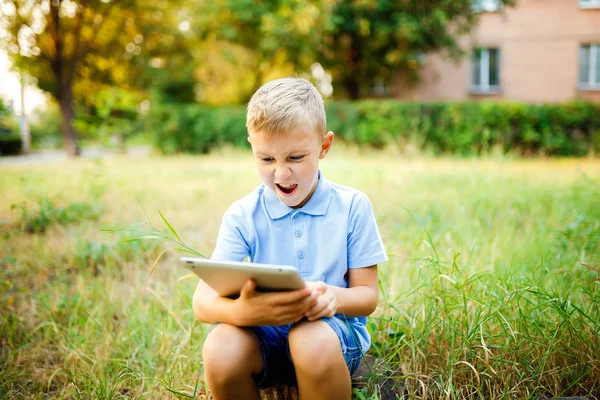 若い子供 sittingin 中庭とタブレット pc でゲームをプレイ. — ストック写真