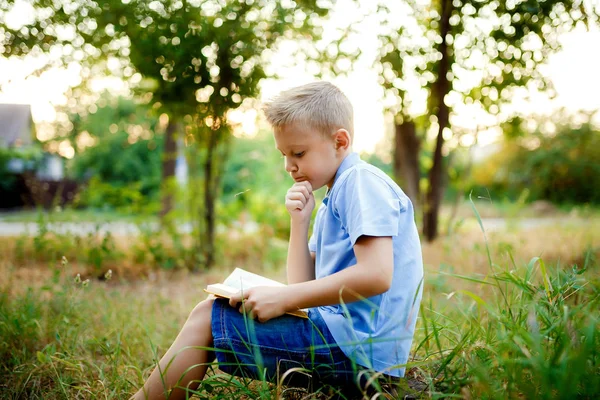 Dziecko siedzi w lesie z książki na kolanach . — Zdjęcie stockowe