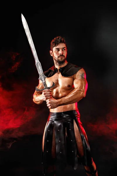 Severe barbarian in leather costume with sword in smoke — Stock Photo, Image