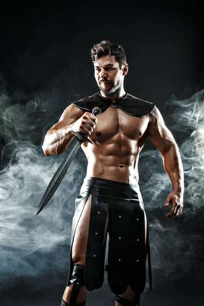 Severe barbarian in leather costume with sword in smoke — Stock Photo, Image