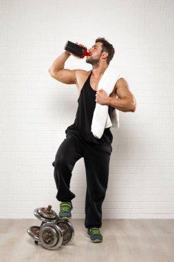 Beyaz arka plan üzerinde yudumlarken gainer bir şişe tutan havlu ile ayakta yakışıklı sporcu.