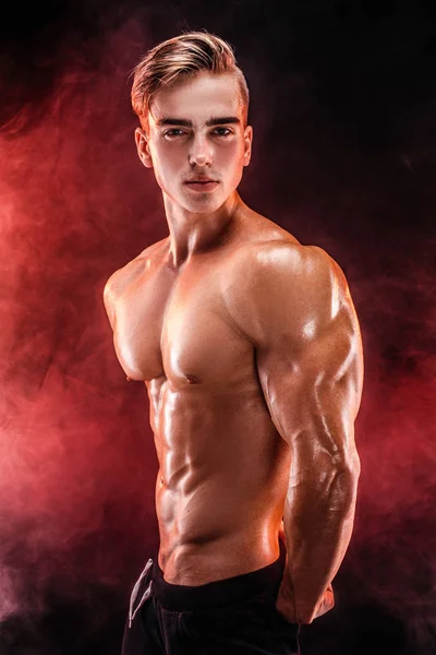 Homme bodybuilder fort avec abdos parfaits, épaules, biceps, triceps, poitrine posant dans la fumée mains en l'air . — Photo
