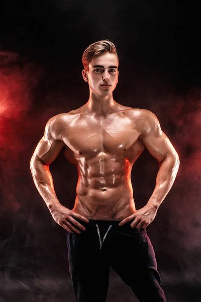 Stark bodybuilder man med perfekta abs, axlar, biceps, triceps, bröst poserar i rök händer upp. — Stockfoto