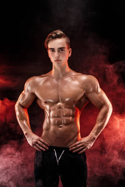 Homme bodybuilder fort avec abdos parfaits, épaules, biceps, triceps, poitrine posant dans la fumée mains en l'air . — Photo