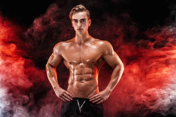 Stark bodybuilder man med perfekta abs, axlar, biceps, triceps, bröst poserar i rök händer upp. — Stockfoto