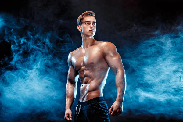 Sterke bodybuilder met zes pack, perfecte abs, schouders, biceps, triceps en borst, persoonlijke fitnesstrainer buigen zijn spieren in rook — Stockfoto