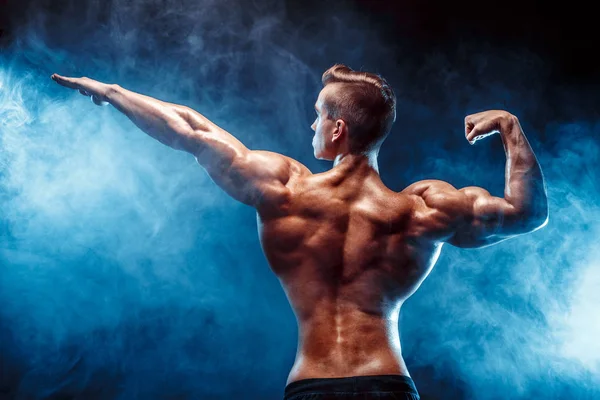 Vista posterior del hombre irreconocible, músculos fuertes posando con el brazo levantado en humo . — Foto de Stock