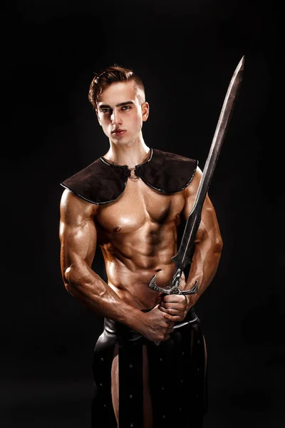 Retrato de guapo gladiador muscular con espada. Aislado. Grabado en estudio. Fondo negro — Foto de Stock