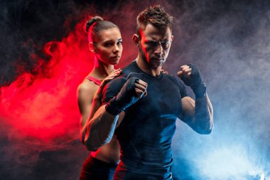 Güçlü boksör yumruklarını üzerinde handwraps ile duruş. Onun arkasında duran kız arkadaşıyla.