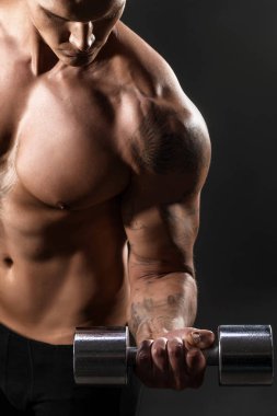 Closeup bir yakışıklı güç atletik erkek vücut dumbbell ile yapıyor. Fitness kas vücut koyu arka plan üzerinde. Seçici odak. Harika vücut geliştirmeci, dövme, poz.
