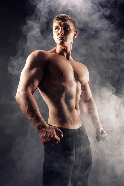 Szép teljesítmény sportos férfi testépítő. Fitness izmos test, sötét füstöt háttér. Tökéletes férfi. Félelmetes testépítő, tetoválás, pózol. — Stock Fotó