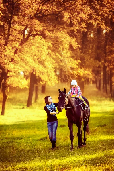 Menina montando em um cavalo com sua mãe andando nas proximidades . — Fotografia de Stock