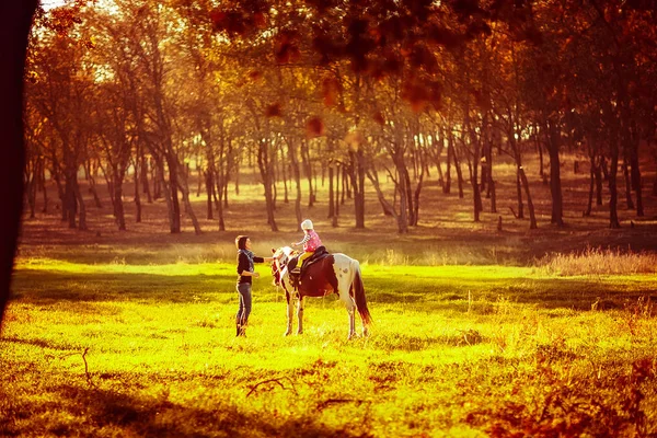 Little girl riding on a horseback with her mother walking nearby. — Stock Photo, Image