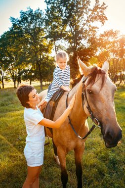 Küçük kız annesiyle yakın duran bir at sırtında tesisi.